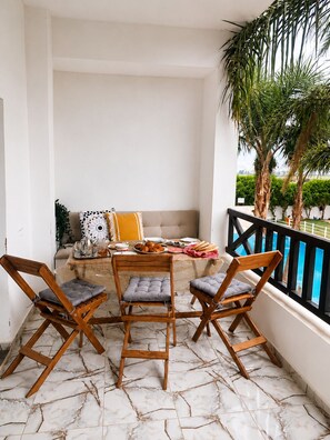 Een balkon met een marmeren vloer, een houten tafel met stoelen en een bank met kussens.