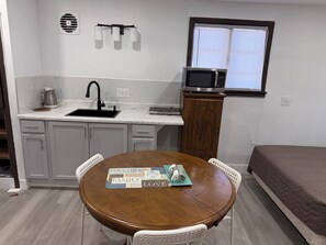 Cocina compacta con lavamanos, microondas y comedor con mesa y sillas.