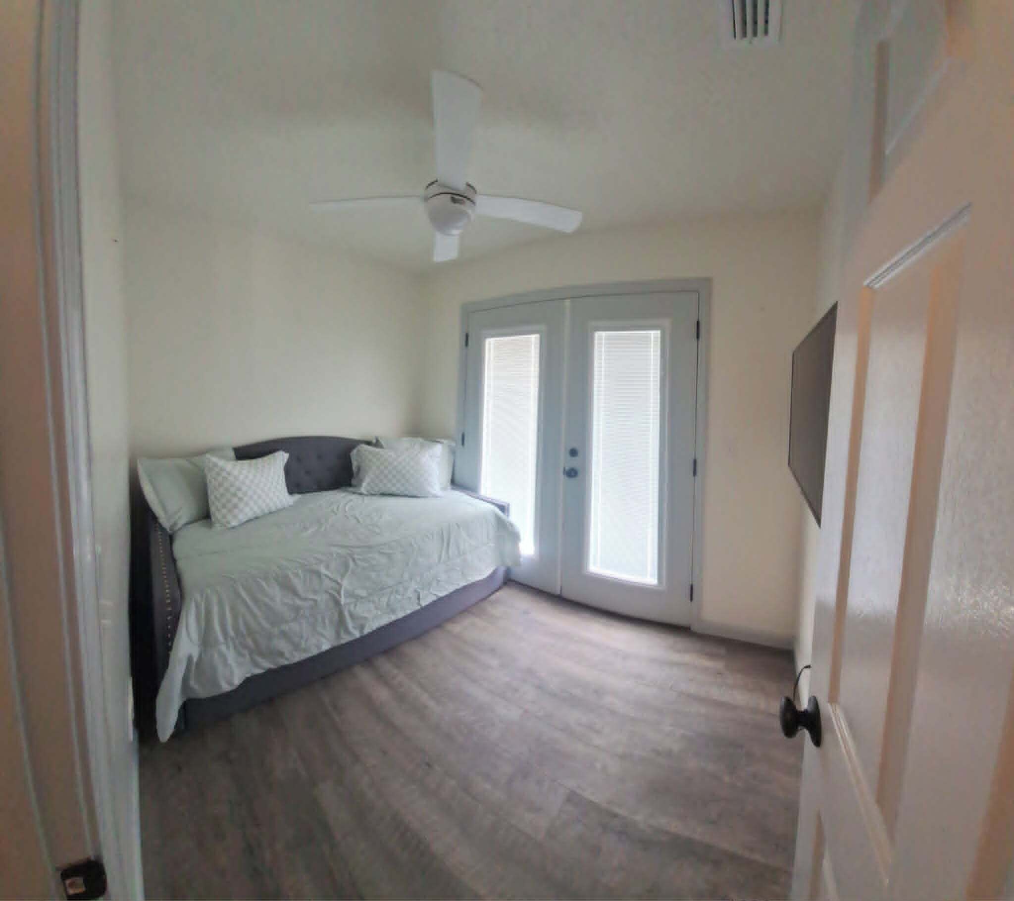 A bedroom with a bed, a ceiling fan, and a door with a window.