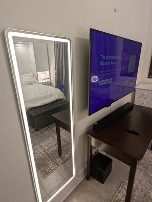 A hotel room with a large mirror, a bed, a TV, and a desk.