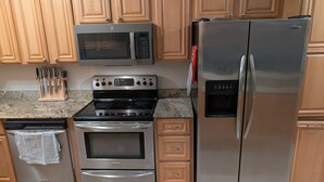 A kitchen with stainless steel appliances, wooden cabinets, and a granite countertop. - The Knickerbocker by Delphius (Tampa)