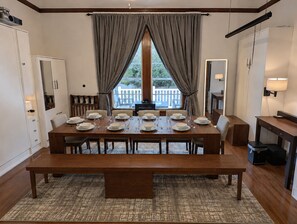 A dining area with a wooden table set for six, flanked by chairs, with a view of a balcony and a window.