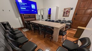 A conference room with a long table and multiple chairs, a television screen displaying a program, and a door leading to another room. - The Knickerbocker by Delphius (Tampa)