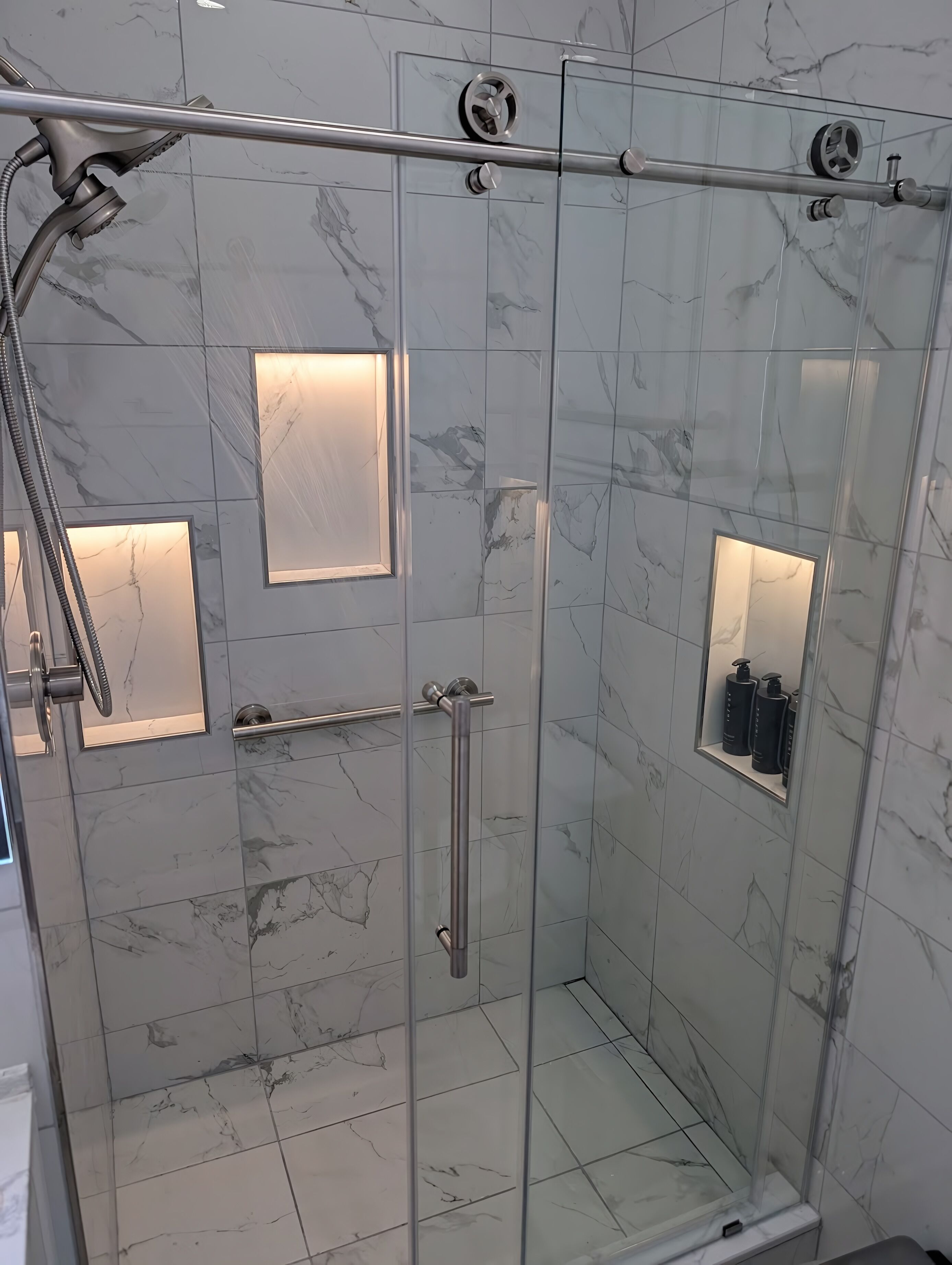 A glass-enclosed shower stall with a handheld showerhead, a handheld shower attachment, and a handheld shower attachment.