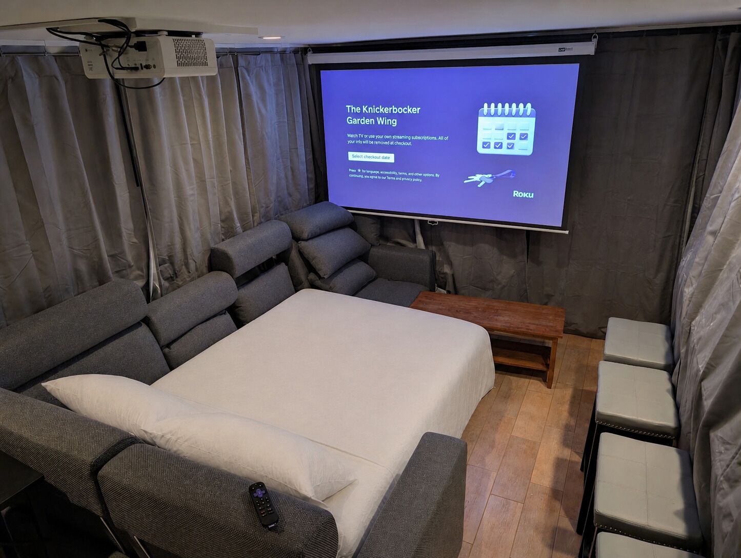 A room with a large bed, a reclining sofa, a small table, and a projector screen displaying a message.