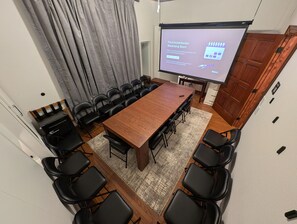 A conference room with a large wooden table, black chairs, a projector screen, and a wooden door.