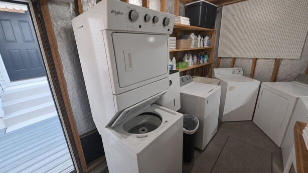 A laundry room with a stacked washer and dryer, a shelf with laundry supplies, and a door leading outside. - The Knickerbocker by Delphius (Tampa)