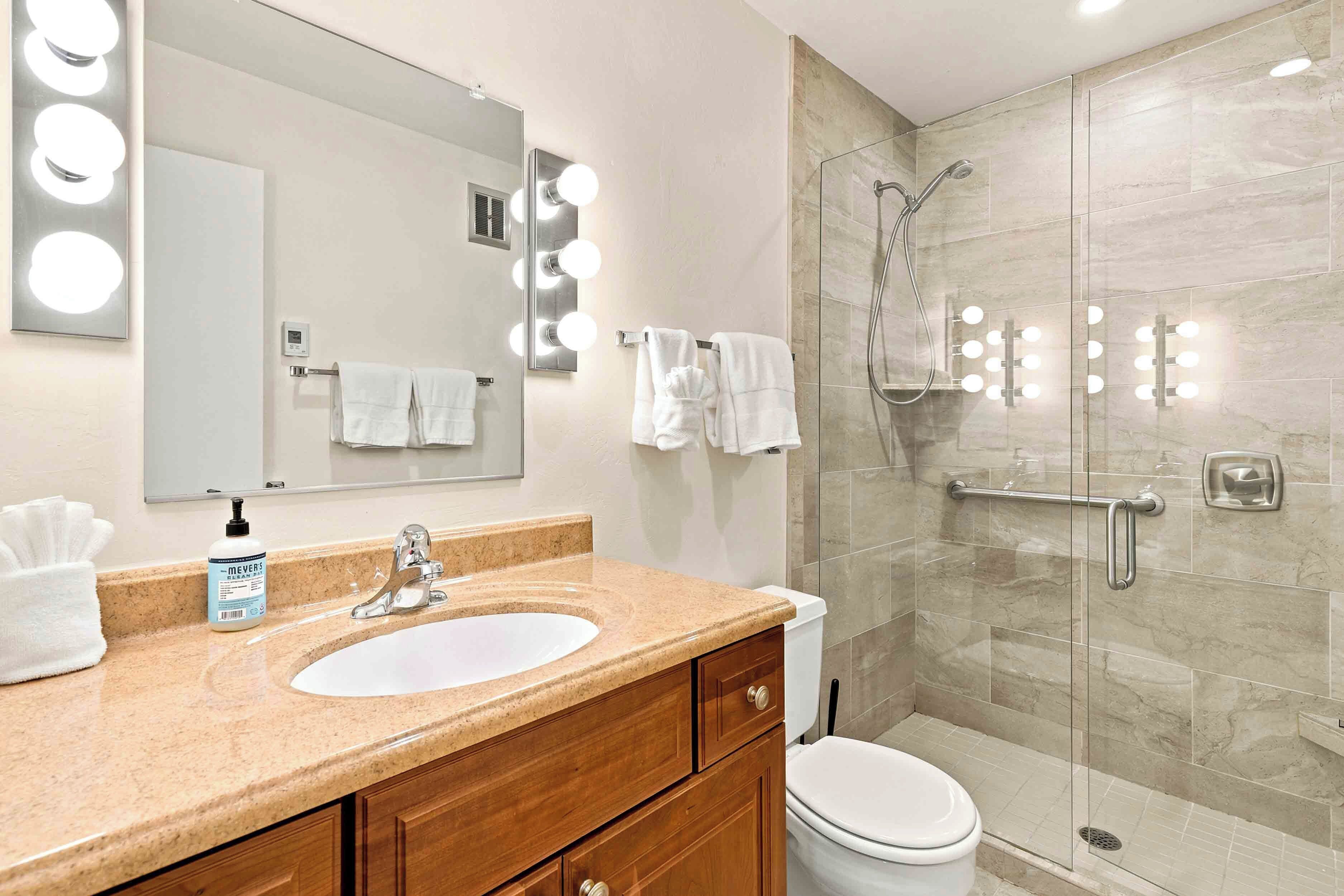 A bathroom with a vanity, sink, mirror, and a glass-enclosed shower with lights.