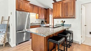 A kitchen with wooden cabinets, a stainless steel refrigerator, granite countertops, and a bar stool area. - Four Seasons Retreat | Minutes to Skiing and Downtown (Ketchum)