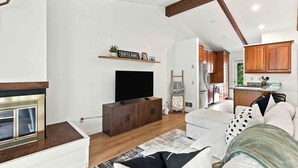 A modern living room with a fireplace, a flat-screen TV, and a kitchen in the background. - Four Seasons Retreat | Minutes to Skiing and Downtown (Ketchum)