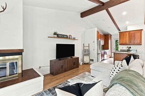 A modern living room with a fireplace, a flat-screen TV, and a kitchen in the background. - Four Seasons Retreat | Minutes to Skiing and Downtown (Ketchum)