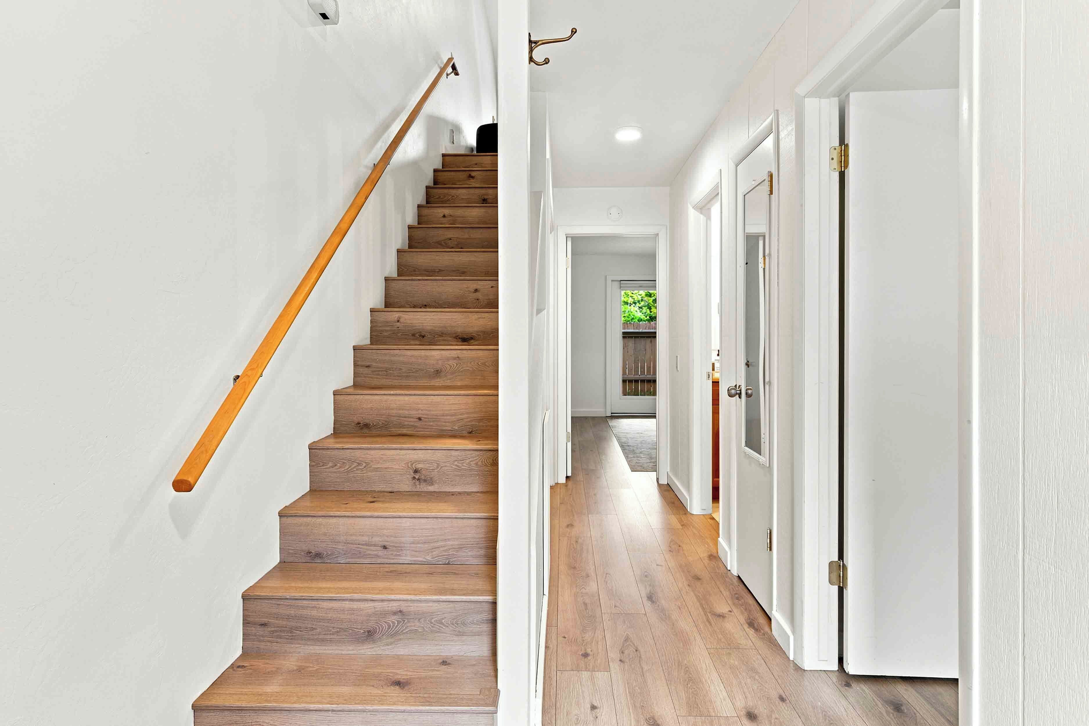 A wooden staircase with white walls and doors, leading to a hallway with a wooden floor.