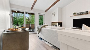 A modern living room with a sofa, a television, and a dining area with a table set for two. - Four Seasons Retreat | Minutes to Skiing and Downtown (Ketchum)