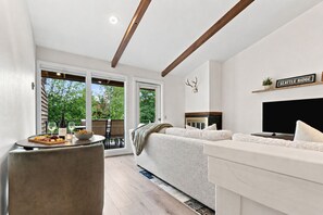 A modern living room with a sofa, a television, and a dining area with a table set for two. - Four Seasons Retreat | Minutes to Skiing and Downtown (Ketchum)
