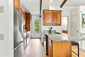A kitchen with wooden cabinets, a stainless steel refrigerator, a granite countertop, and a view of a balcony. - Four Seasons Retreat | Minutes to Skiing and Downtown (Ketchum)