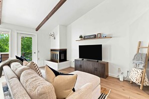 Uma sala de estar com sofá, televisão, lareira e um chifre de veado na parede.