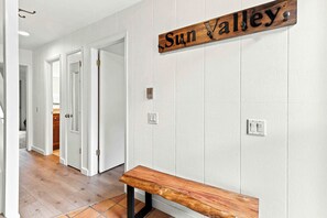 A hallway with a wooden bench, a door with a brass handle, and a wall-mounted sign that reads 'Sun Valley.' - Four Seasons Retreat | Minutes to Skiing and Downtown (Ketchum)