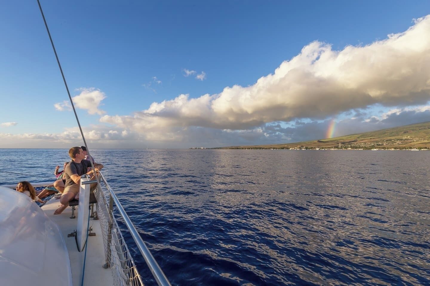 Un bateau transportant des passagers qui admirent le paysage marin et un arc-en-ciel lointain.