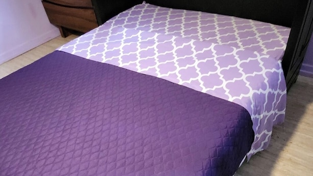 A bed with a patterned mattress and a quilted bedspread. - Central Maui Studio • Kitchenette + Queen Bed (Wailuku)