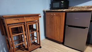 A kitchen with a wooden cabinet, a stainless steel refrigerator, and a microwave on the countertop. - Central Maui Studio • Kitchenette + Queen Bed (Wailuku)