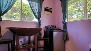 Ein Zimmer mit einem kleinen Tisch, einem Stuhl, einem Kühlschrank und einem fenster mit Vorhängen.