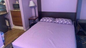 Un letto singolo con testiera, un comodino con una lampada e un piccolo settimino in legno.