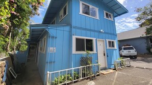 Un edificio a due piani con facciata blu, una porta ben visibile e un piccolo recinto con piante.