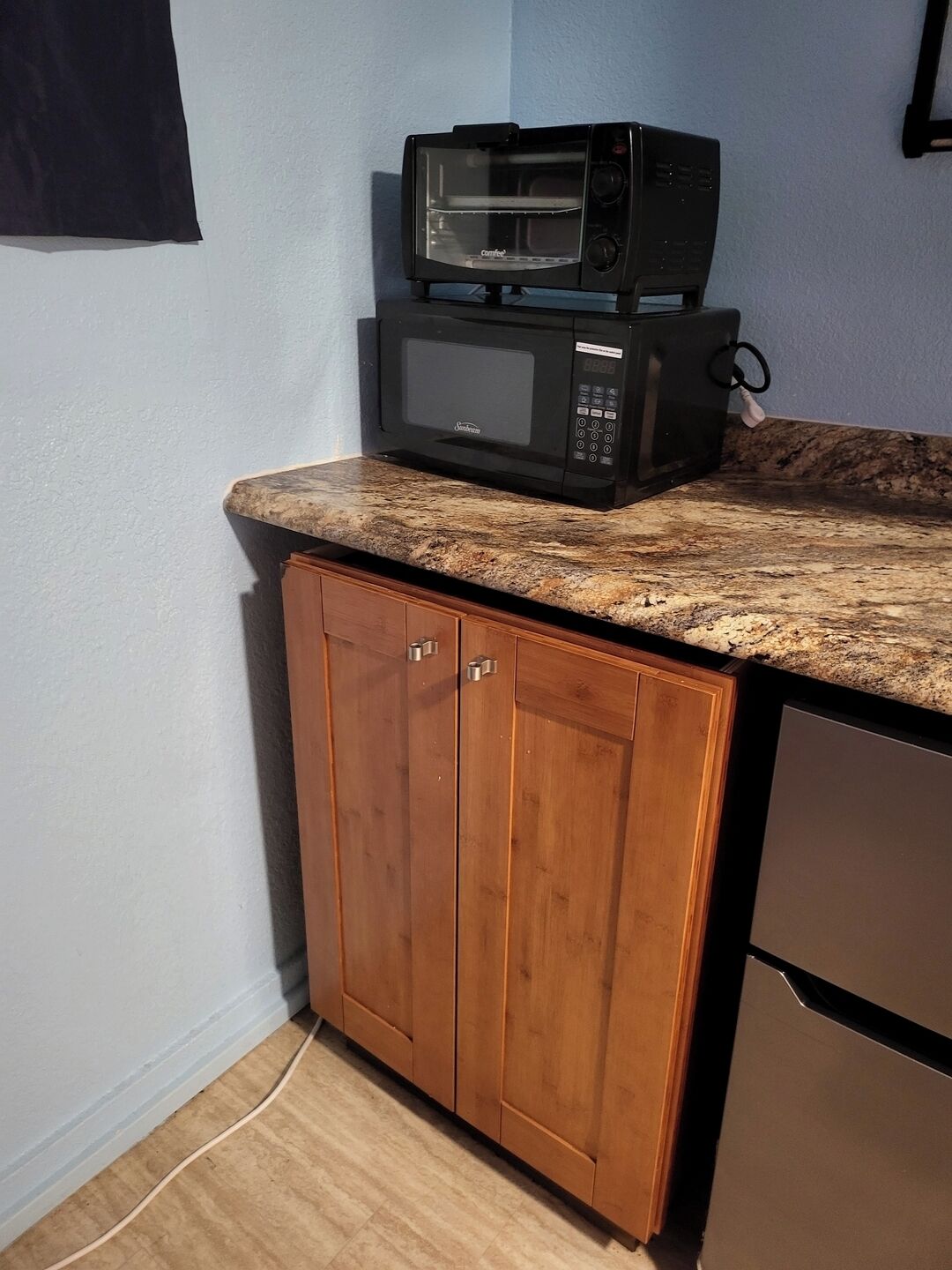 Eine Küche mit Mikrowelle und Toaster auf der Arbeitsplatte, Holzschränken und einem Edelstahl-Kühlschrank.