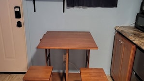 Una cucina compatta con un tavolo in legno e due sgabelli, una finestra con tende e una porta con serratura.