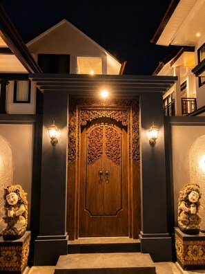 Una entrada oscura con puerta de madera adornada con intrincados grabados y dos luces empotradas.