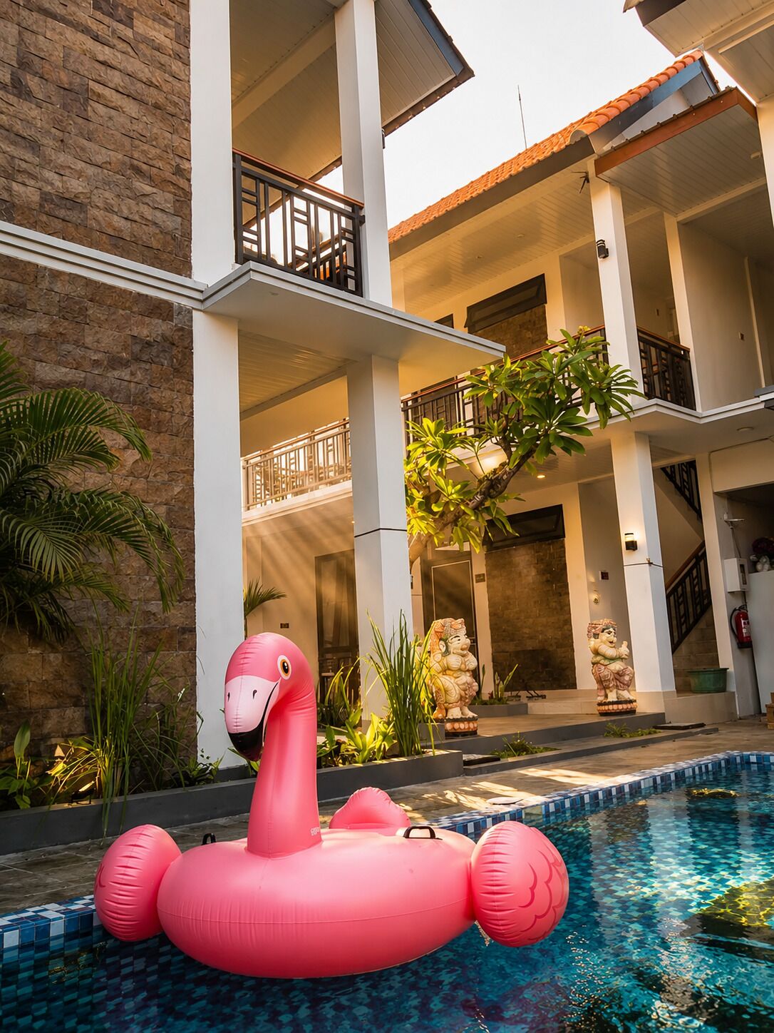 Una piscina con un flamenco inflable rosa, rodeada por un edificio de fachada de piedra y varios balcones.