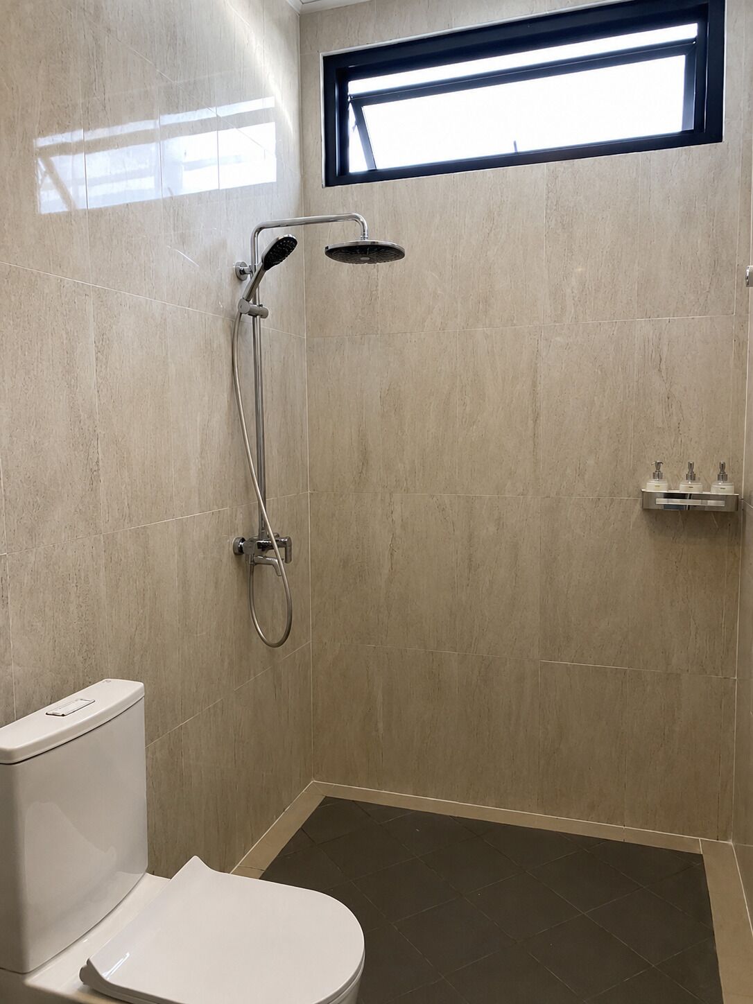 A bathroom with a toilet, a shower with a handheld showerhead, and a window above the shower.