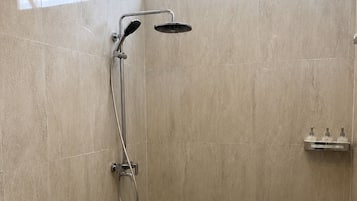 A bathroom with a toilet, a shower with a handheld showerhead, and a window above the shower.
