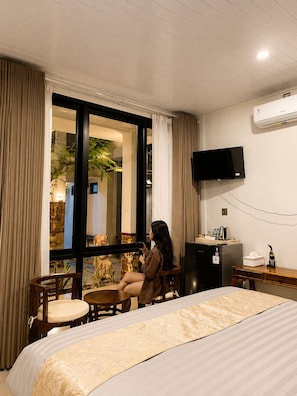 Habitación de hotel con cama, escritorio, silla, televisión y ventana con cortinas.