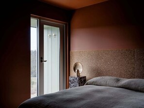 A bedroom with a bed, a nightstand, and a door leading to a balcony.