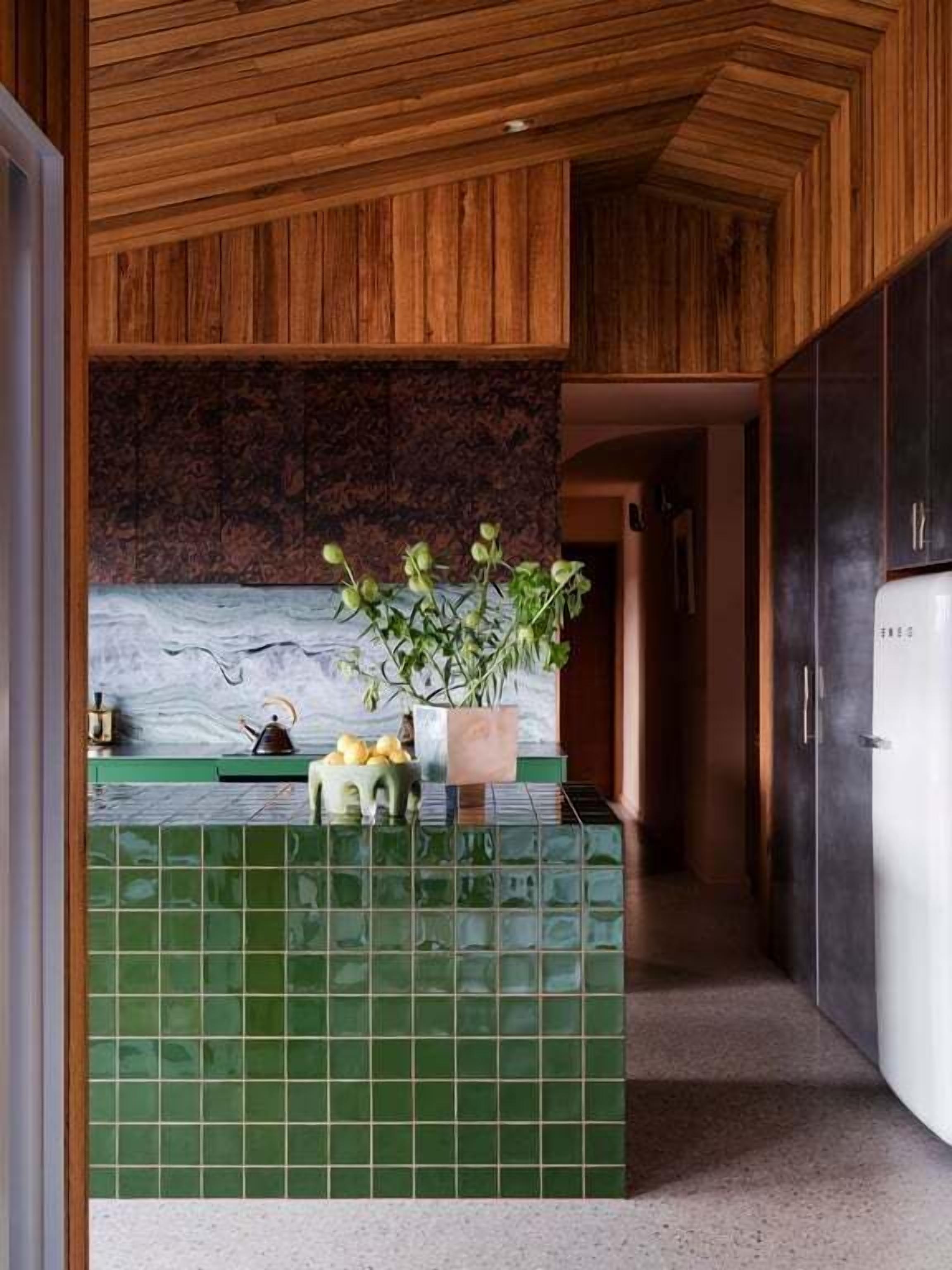 A kitchen with a green tiled backsplash, wooden ceiling, and a refrigerator.