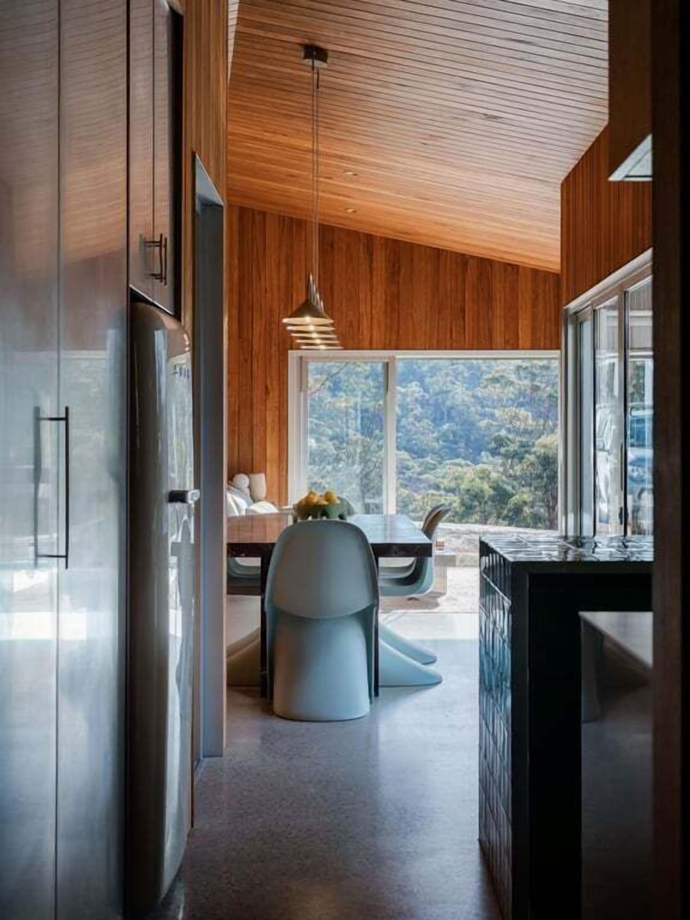 Uma cozinha moderna com teto de madeira, uma área de jantar com mesa e cadeiras, e vista para o exterior.
