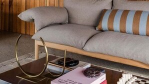 A room with a wooden paneled wall, a grey sofa with striped cushions, a round table with books and a globe, and a floor lamp. - Threefold - Freycinet Luxury Hosts (Swansea)