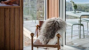 A room with a wooden ceiling, a large window, and a chair with a fur throw. - Threefold - Freycinet Luxury Hosts (Swansea)