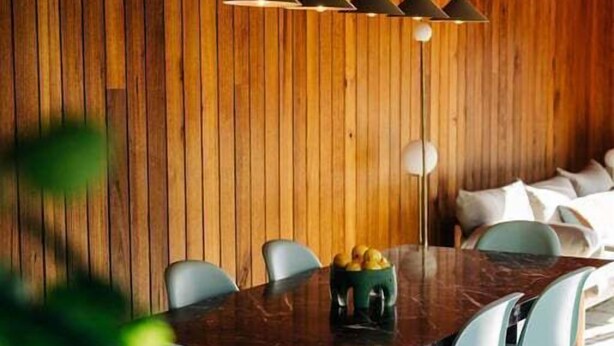 A dining area with a wooden wall, a dark wooden table, and light blue chairs. - Threefold - Freycinet Luxury Hosts (Swansea)