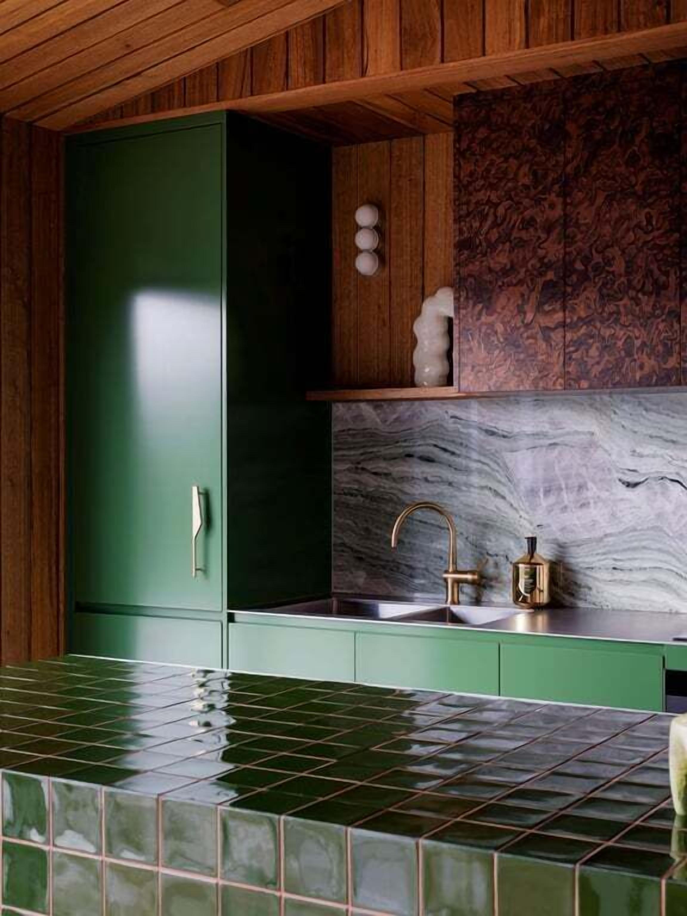 A kitchen with green cabinets, a marble backsplash, and a tiled countertop.