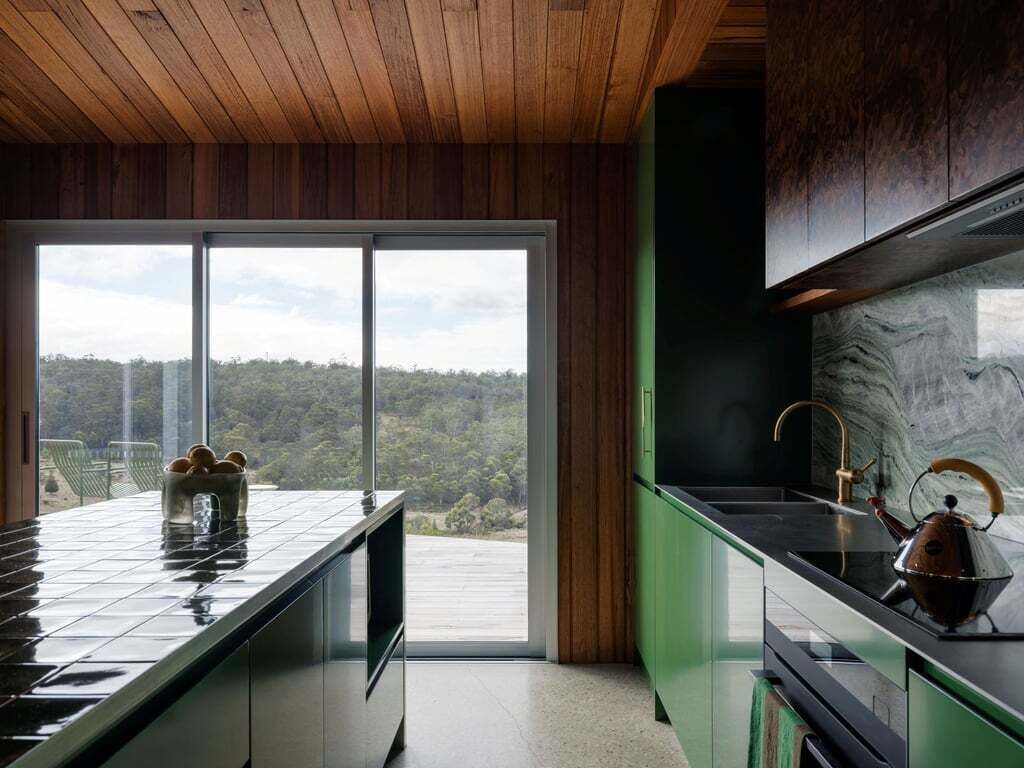 A modern kitchen with a large window, a green countertop, and a kettle.