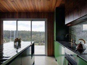 A modern kitchen with a large window, a green countertop, and a kettle.