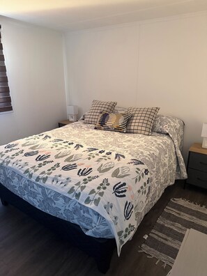 A bedroom with a bed, nightstands, a bedside table, and a patterned bedspread.