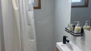 Casa de banho com cortina de chuveiro, lavatório com espelho e produtos de higiene numa estante.