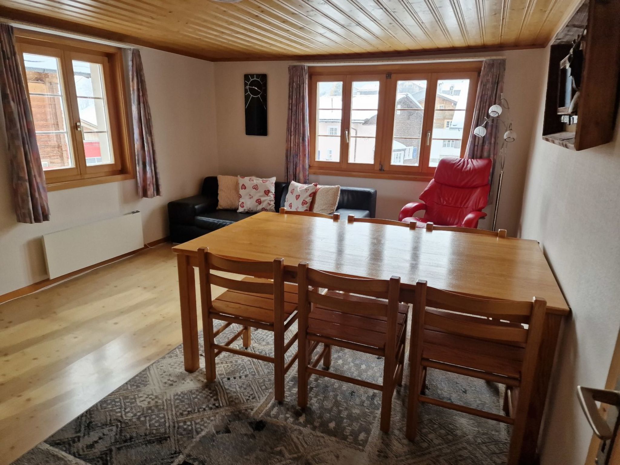 A dining area with a wooden table and chairs, a black sofa with patterned cushions, and a red chair.