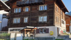 A multi-story wooden building with balconies and windows, a small entrance area with a door, and a visible mailbox. - Via Cuort, Brigels, (Breil/Brigels), 65083B by Interhome (Breil/Brigels)