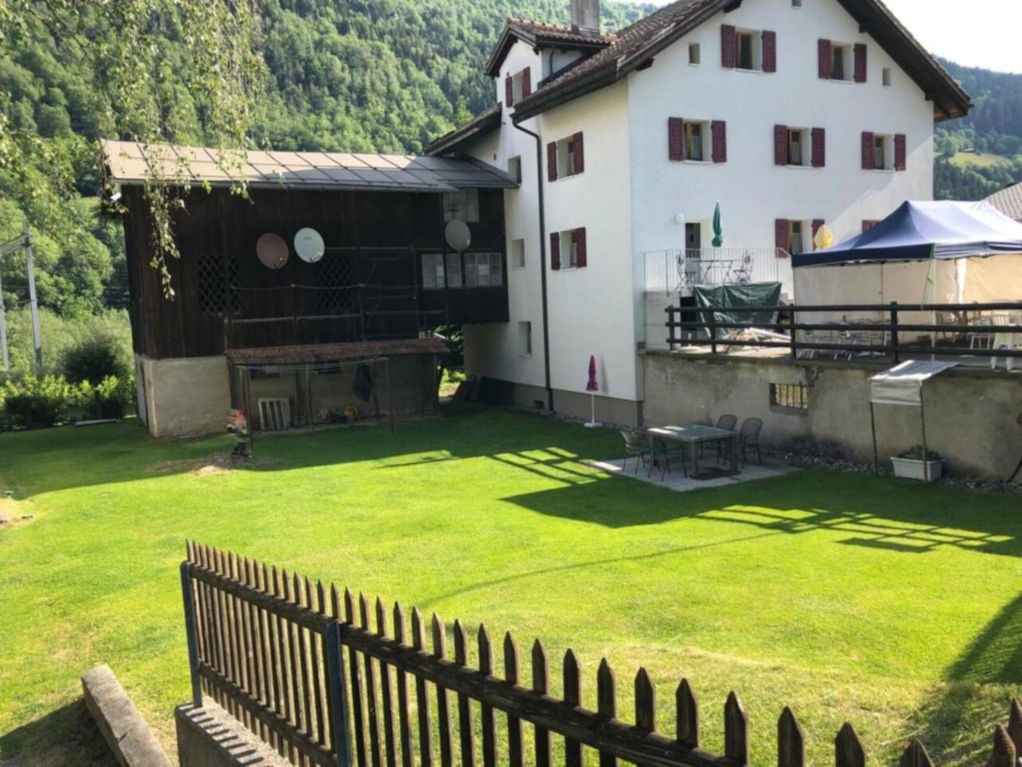 Ein zweistöckiges Haus mit umzäuntem Garten, einem Grillplatz und einem Tisch mit Sitzgelegenheit draußen.