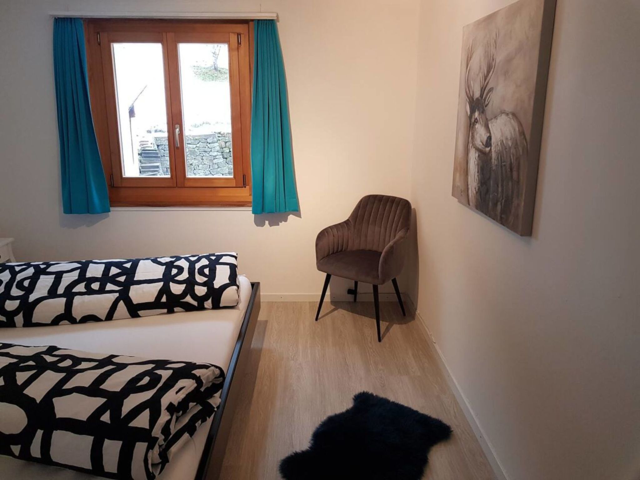 Ein Zimmer mit einem Bett, einem Sessel, einem Fenster mit Vorhängen und einem Bild an der Wand.