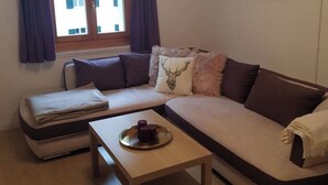 Ein modernes Wohnzimmer mit einer Eckcouch, einem kleinen Holztisch und einem Fenster mit Vorhängen.
